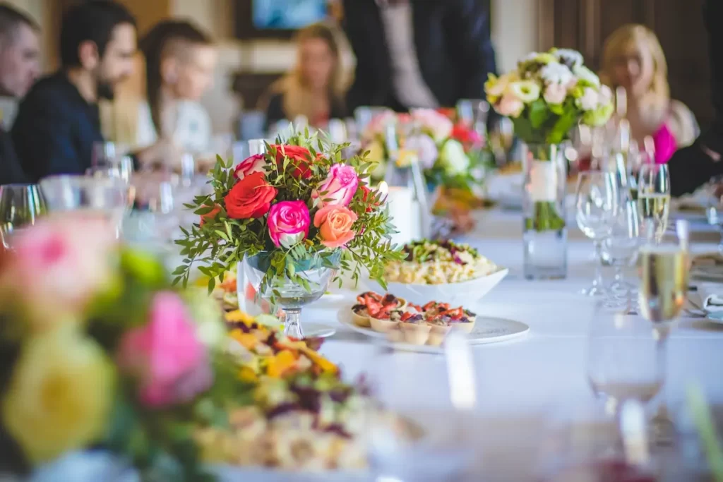 گل ها و شیرینی هایی که بر روی میز قرار دارند و مردم نیز به دور میز نشسته اند