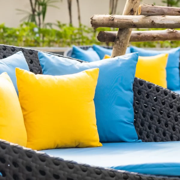 صندلی های راحتی که دارای تشک آبی با بالشتک های زرد و ابی میباشد و در فضای باز قرار دارد