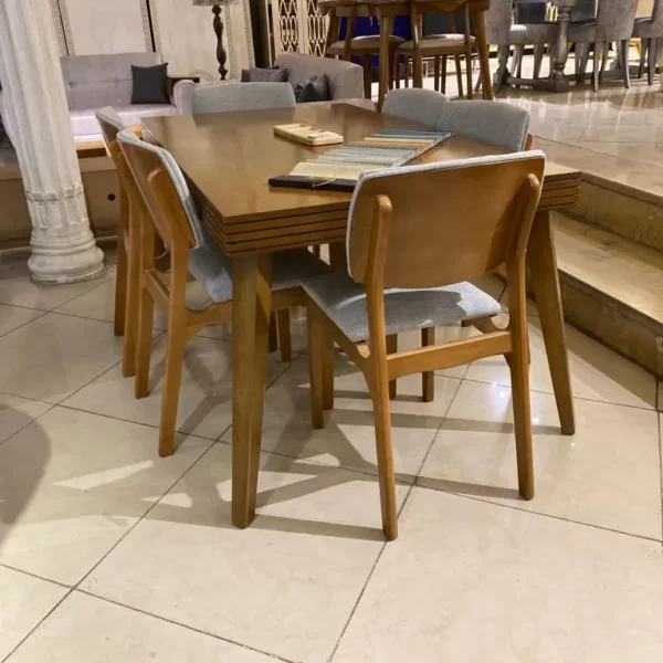 میز نهارخوری شیش نفره چوبی که صندلی ها در اطراف آن گذاشته شده است و در اطراف میز هم مبل ها قرار دارد