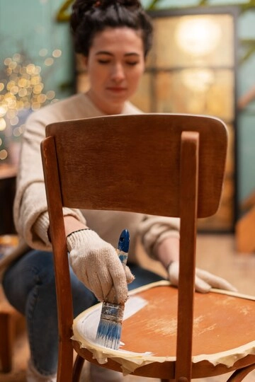 زن جوان در حال رنگ سطح چوبی صندلی